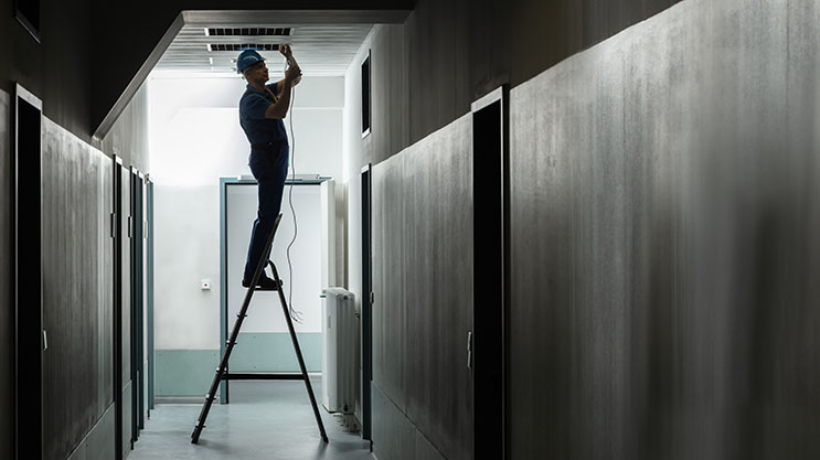 An electrician performing preventative maintenance on a business's lighting systems.
