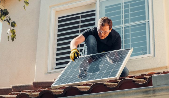 An electrician installing a solar panel on a home's roof.