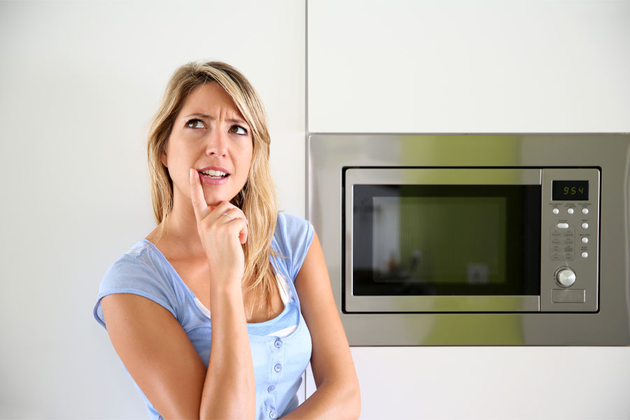 Confused woman in front of a microwave